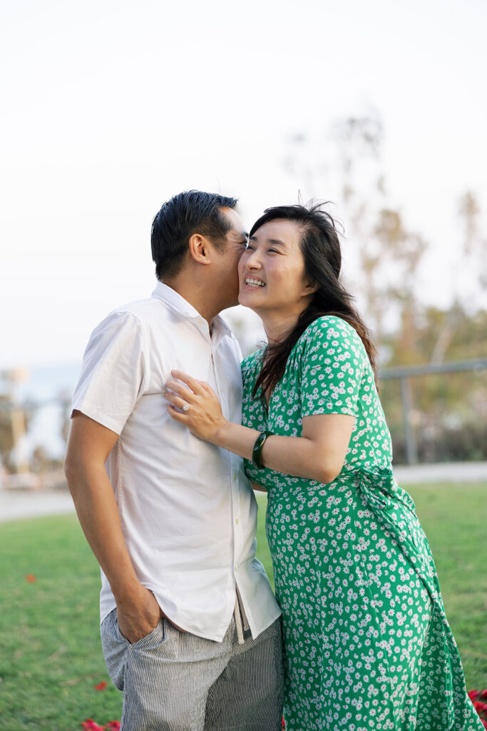 Woman smiling while man kisses her cheek during engagement photo session with Orange County proposal photographer.