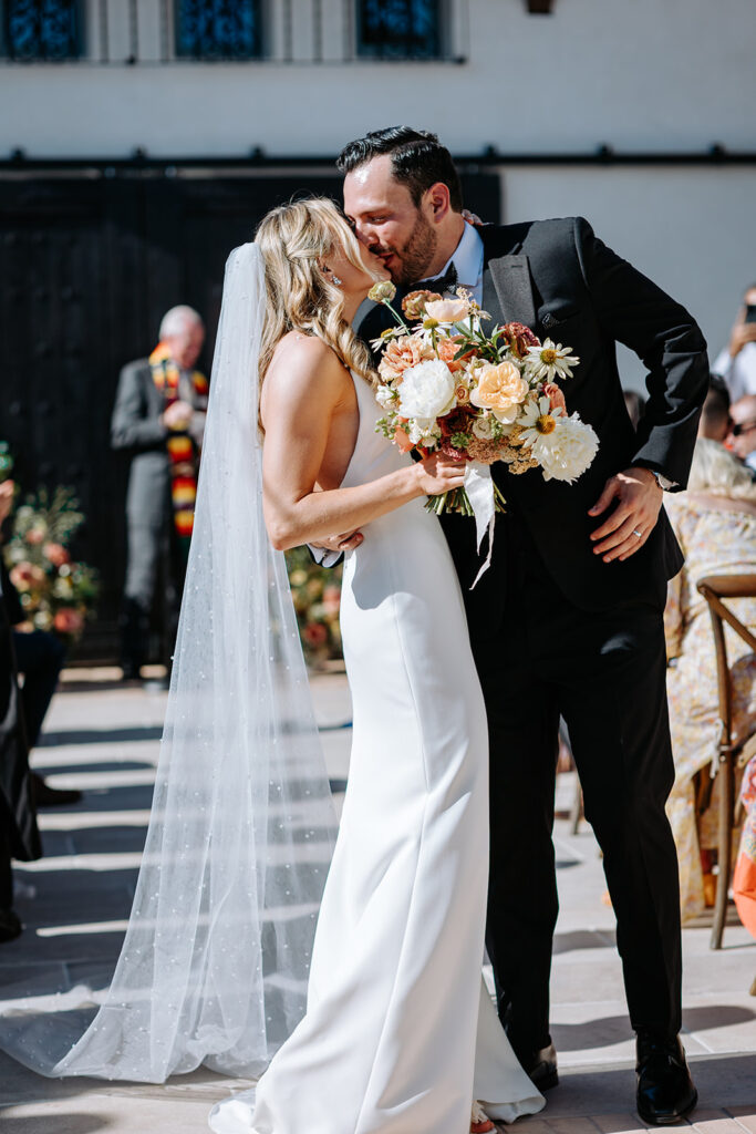 bride and groom sharing a kiss while leaving ceremony at wedding at agape 1928 in san clemente