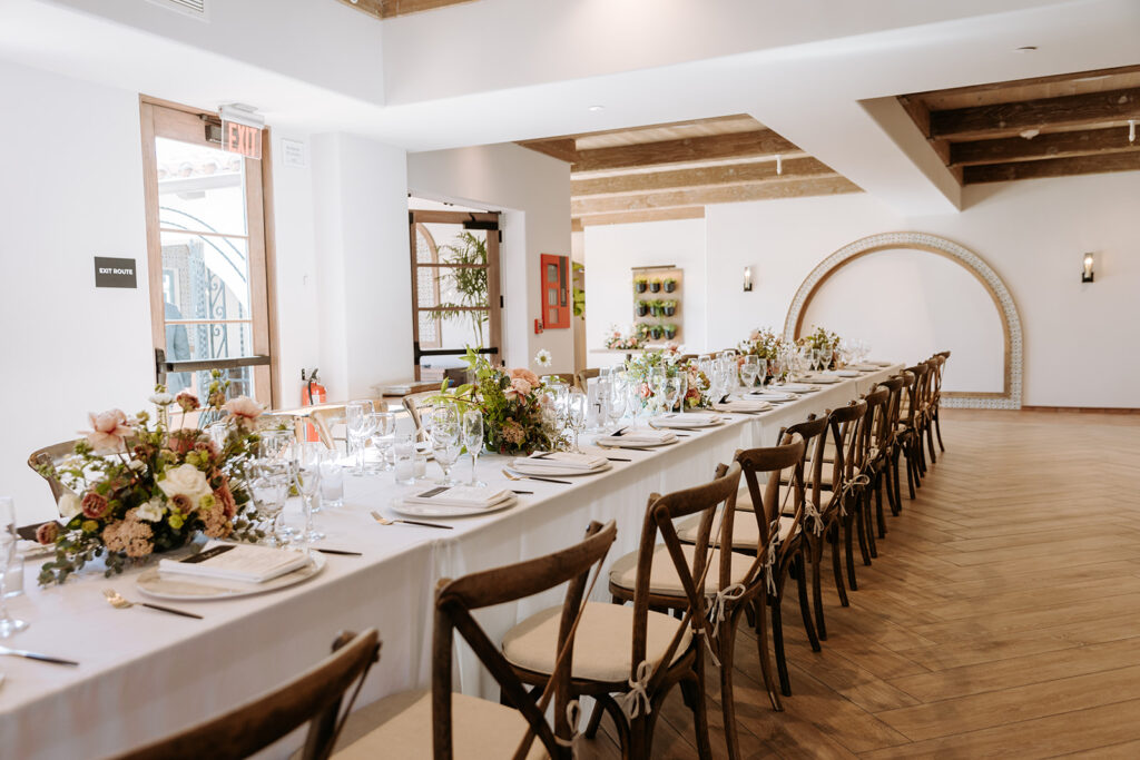 rectangular tables set up with simple white linens and tableware and lush floral arrangements for wedding reception