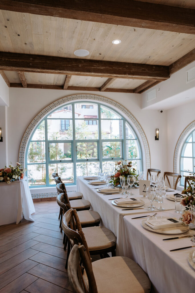 rectangular tables set up with simple white linens and tableware and lush floral arrangements for wedding reception