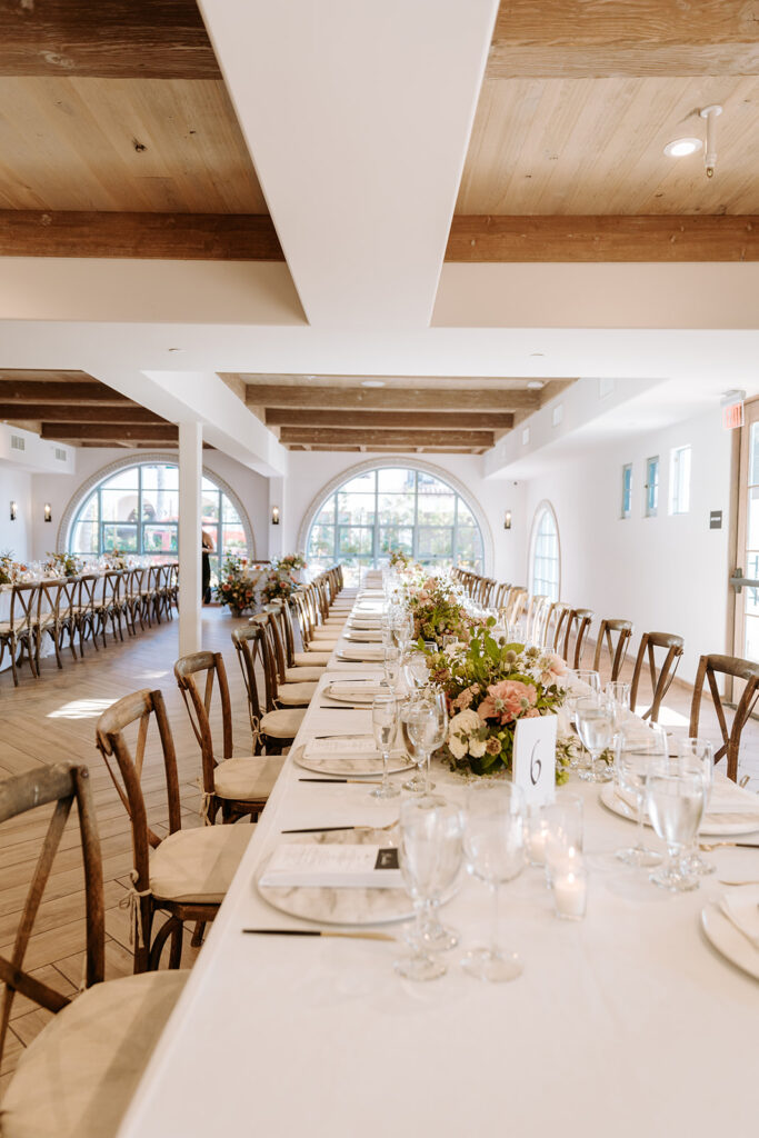 rectangular tables set up with simple white linens and tableware and lush floral arrangements for wedding reception