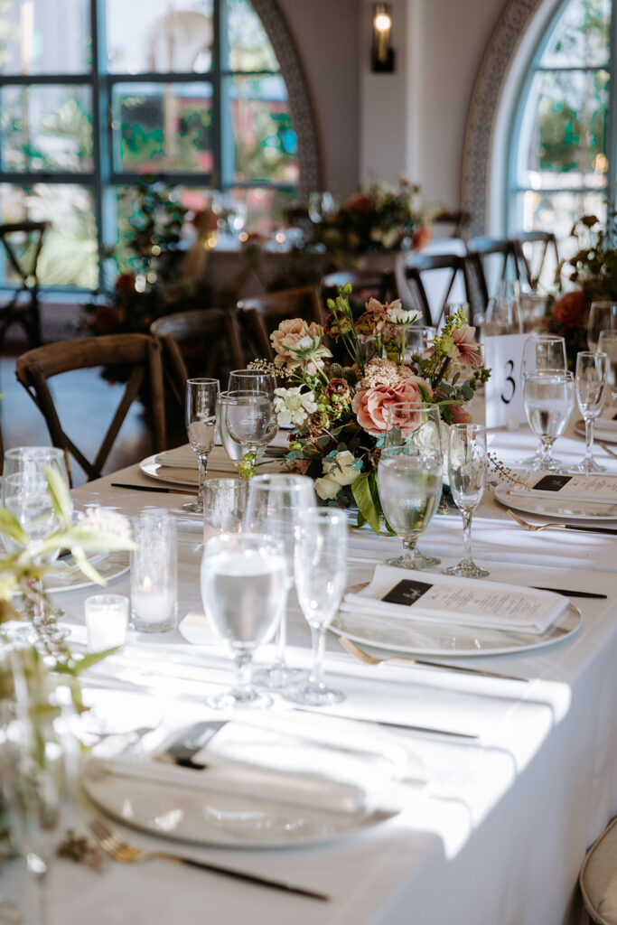 close up of tablescape set up with simple white linens and tableware and lush floral arrangements for wedding reception