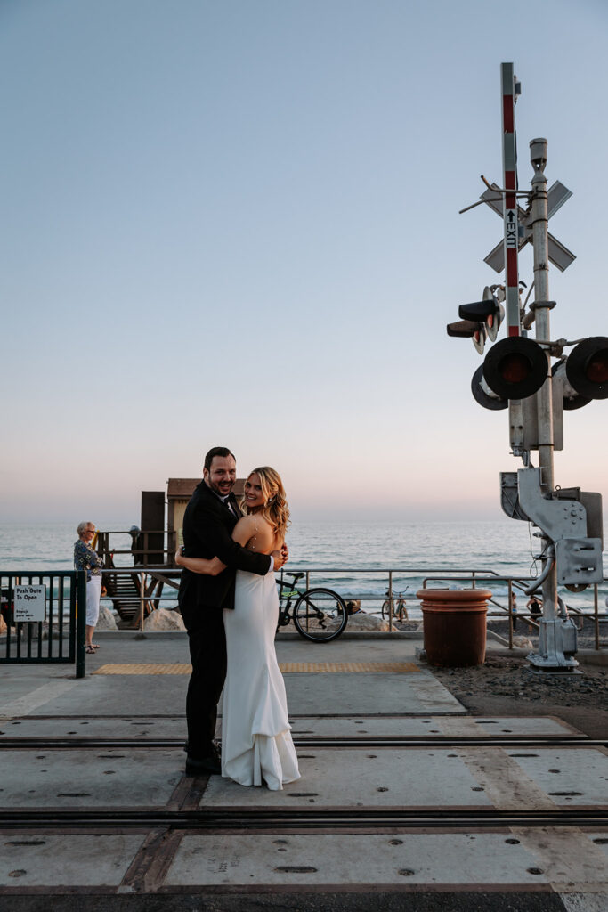 bride and groom golden hour photos by railroad crossing and ocean in the background