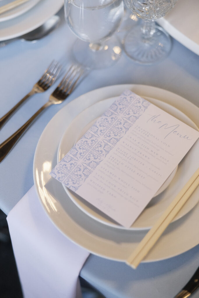 white and blue patterned menu sits on top of white plates and blue tablecloth