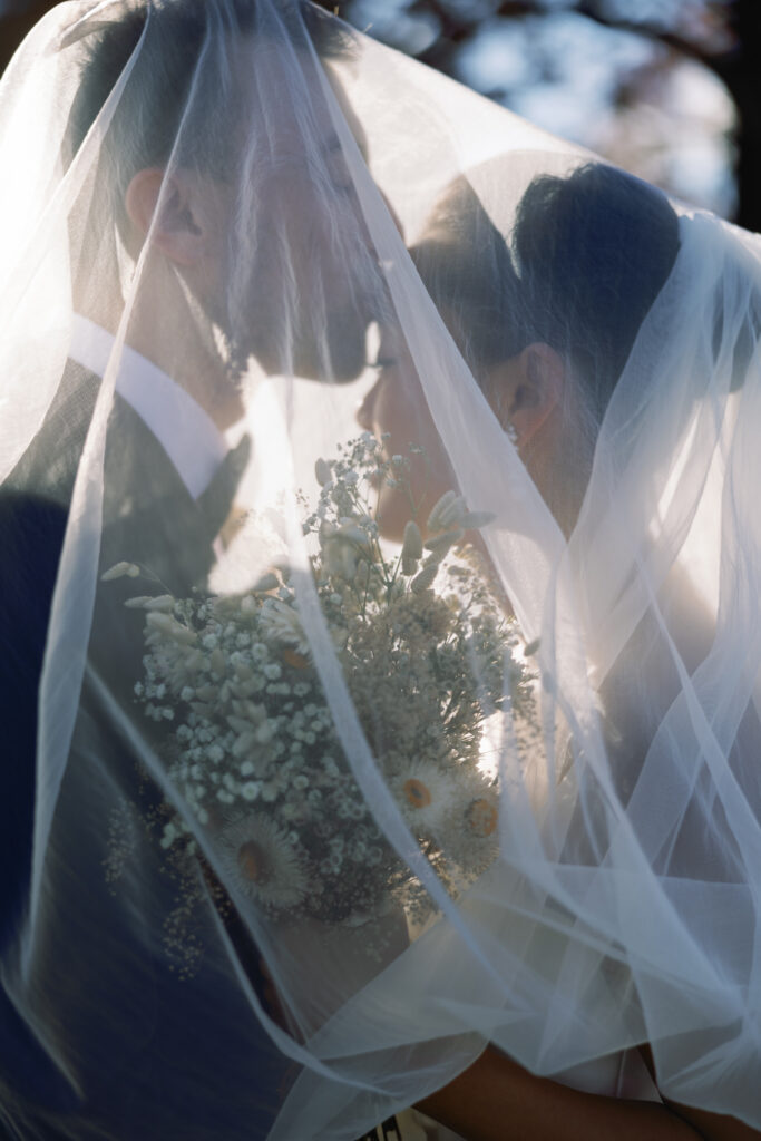 groom kisses his brides forehead while under her veil and she is holding her bouquet 