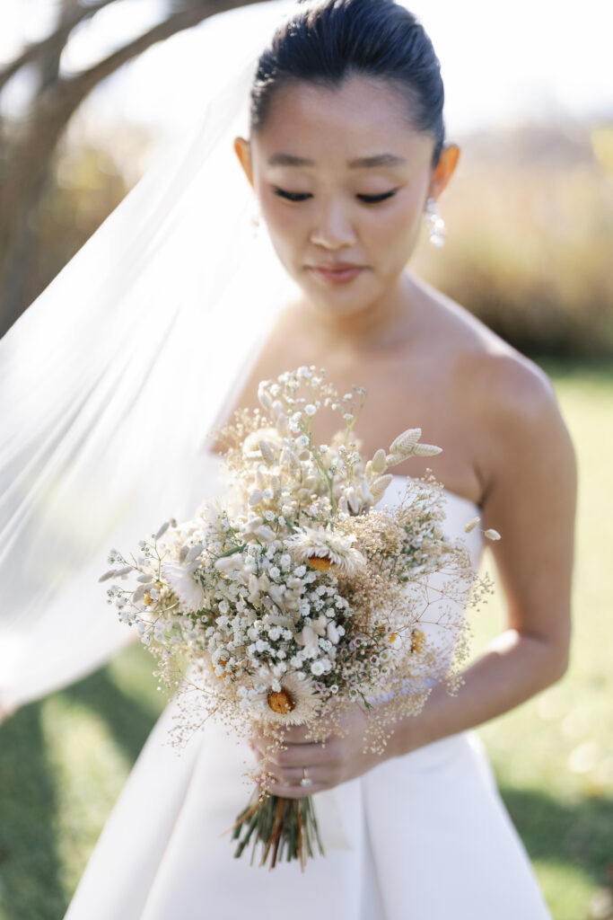 bride holding a bridal bouquet of pink daisies, baby’s breath, and dried grass | 2025 wedding trends