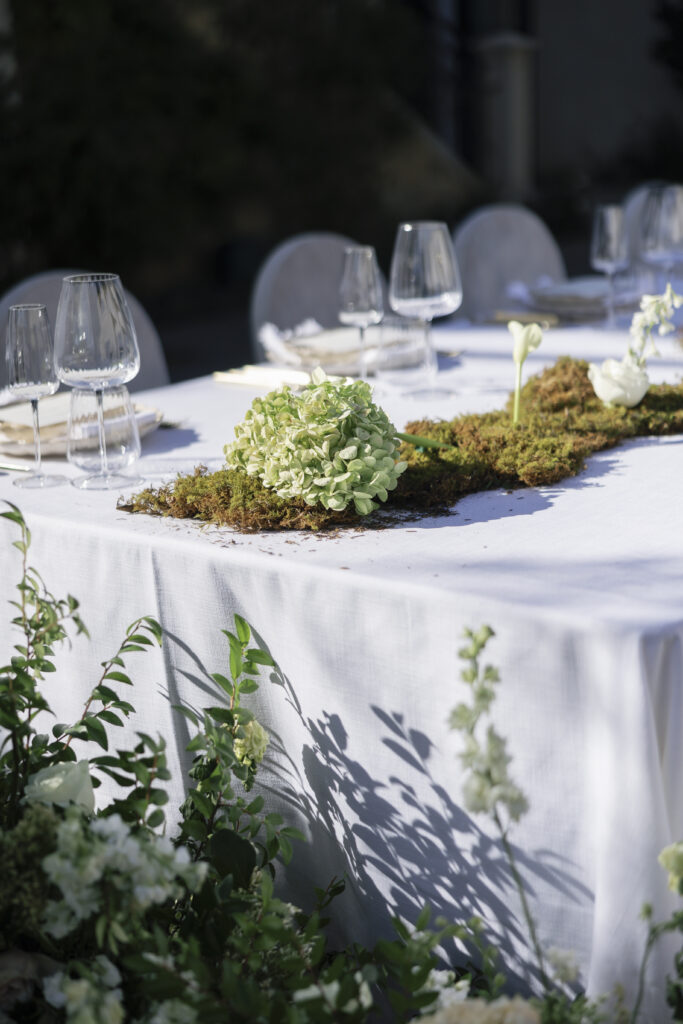 A reception table adorned with natural moss, white blooms, and greenery