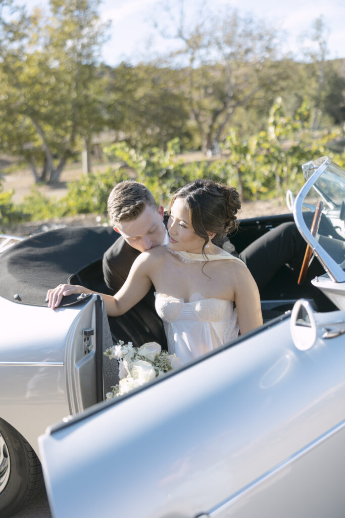 bride and groom outside during golden hour sitting inside of their get away convertable 