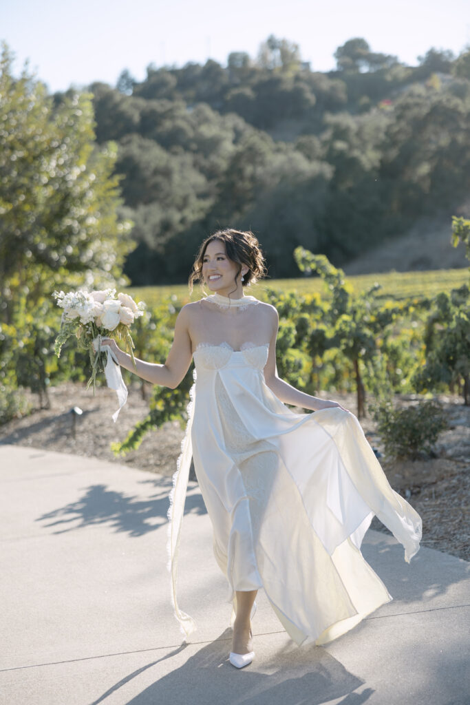 a bride outside during golden hour holding up her minimal length dress and bouquet