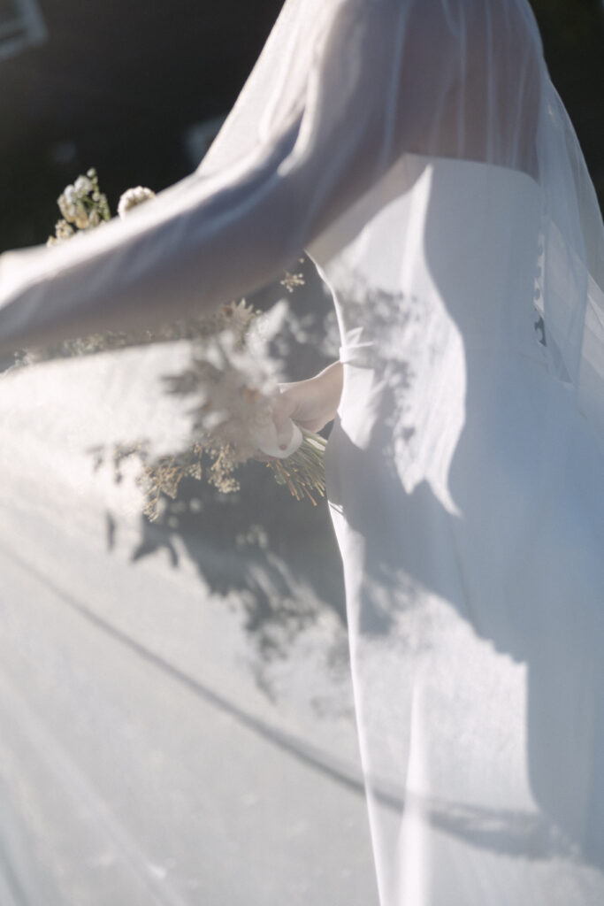 a bride wearing a flowing sheer veil and delicate bouquet with white blooms | 2025 wedding trends