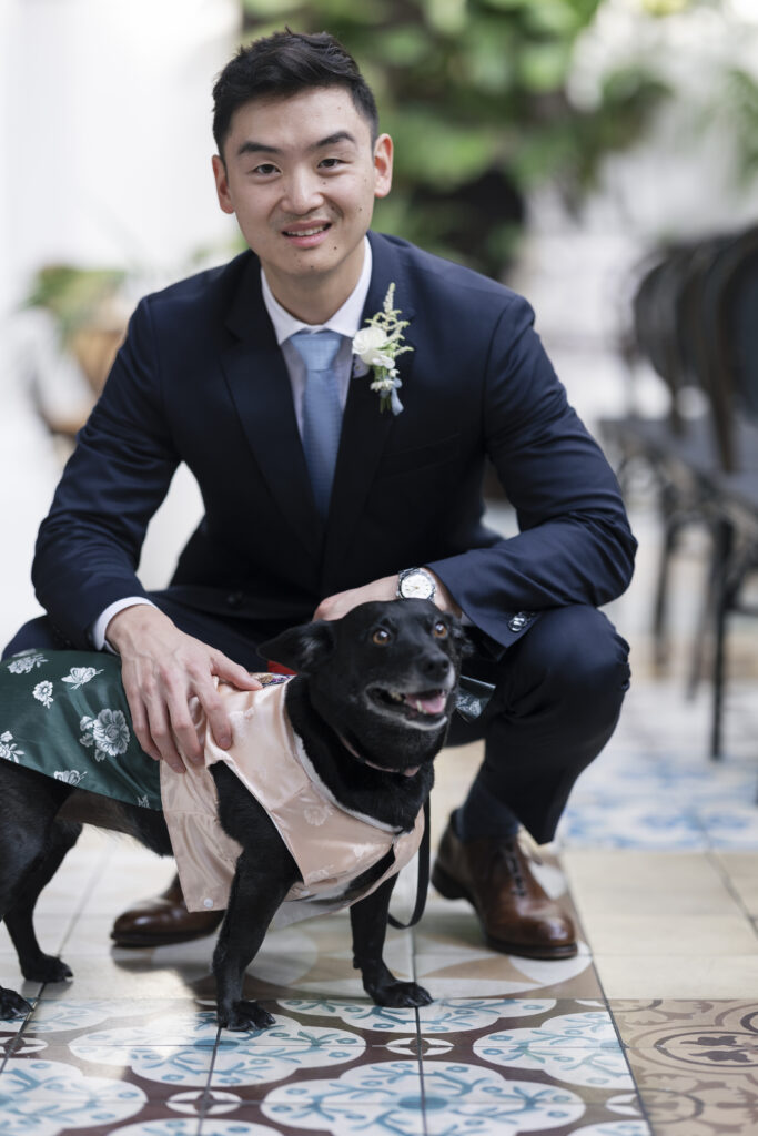 groom posing with his dog. dog is dressed in a cute pink outfit