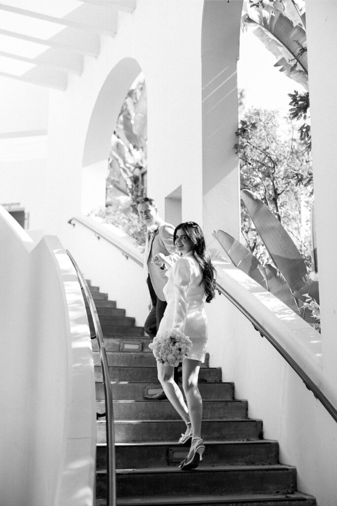 The bride and groom walk up elegant stairs, capturing a candid moment at their Beverly Hills Courthouse wedding.
