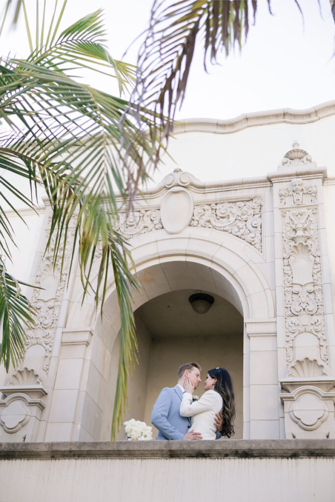 Standing under a grand arch with intricate details, the couple shares a tender moment at their courthouse elopement.