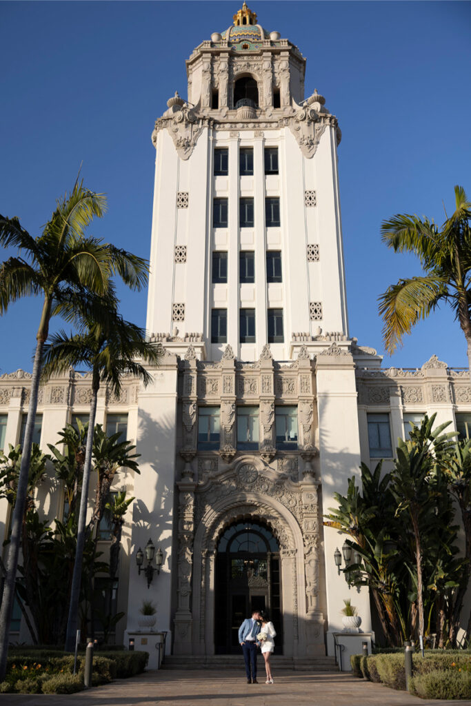 A wide-angle view showcases the Beverly Hills Courthouse as the couple enjoys a romantic moment outside.