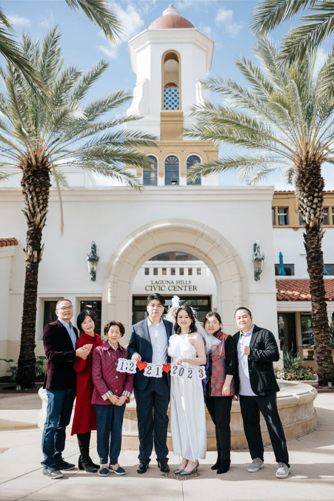 Bride and groom stand with their family in front of Laguna Hills Civic Center after city hall elopement in Orange County. 