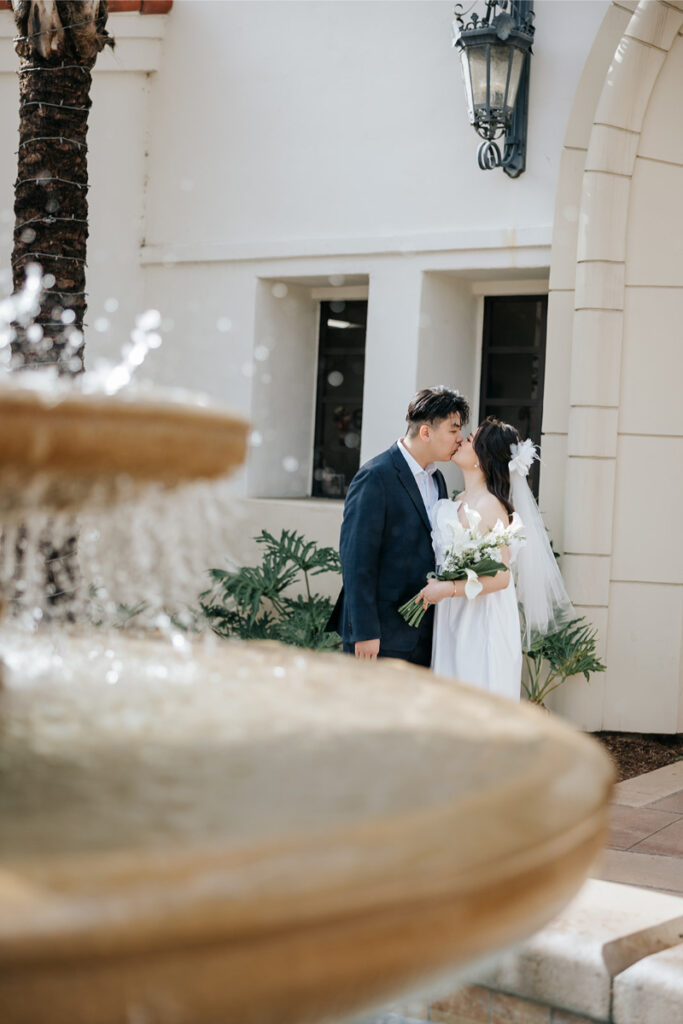 Bride and groom share kiss with a beautiful water fountain in the foreground. 