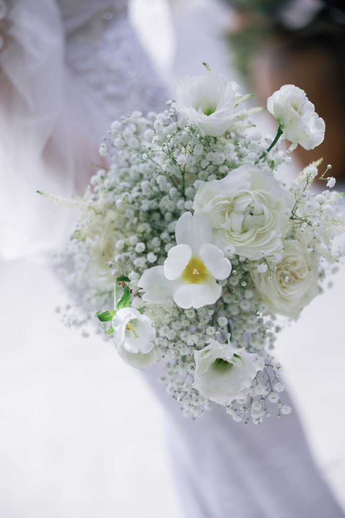 A stunning bouquet of white flowers, including roses and baby's breath, held by a bride.