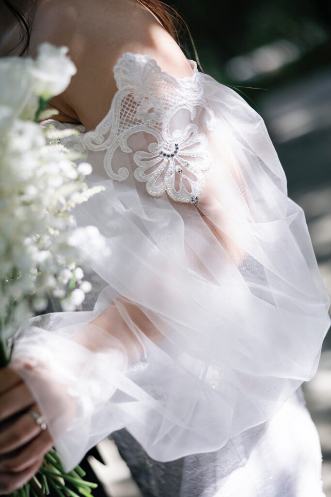 Close up of lace detail on a wedding dress sleeve illuminated in soft sunlight.