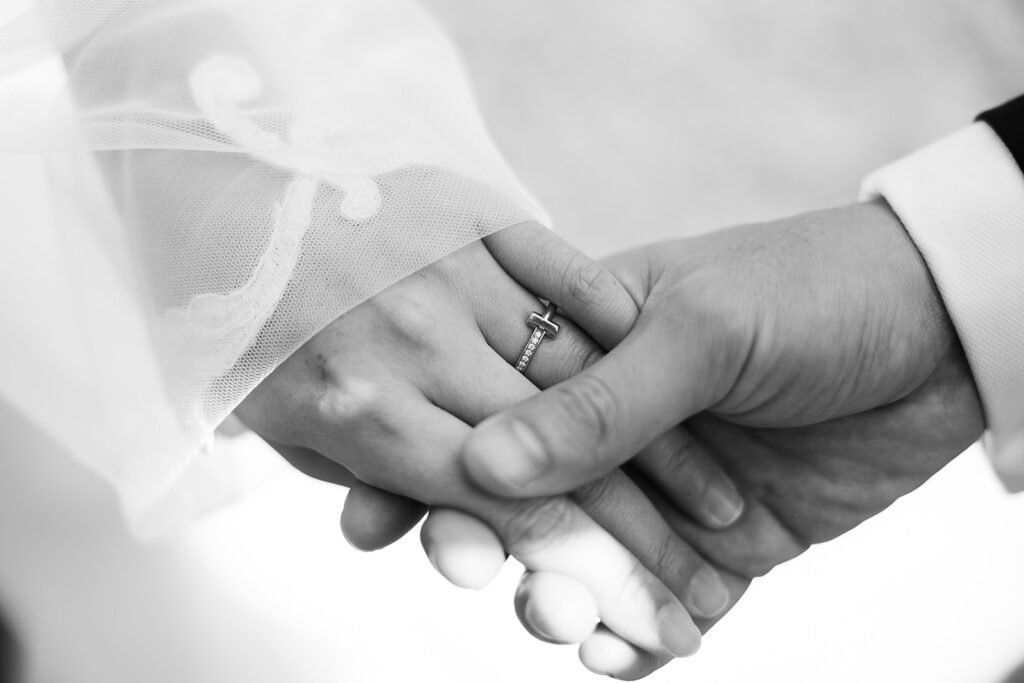 Black and white close-up of a couple holding hands, highlighting the bride’s engagement ring.