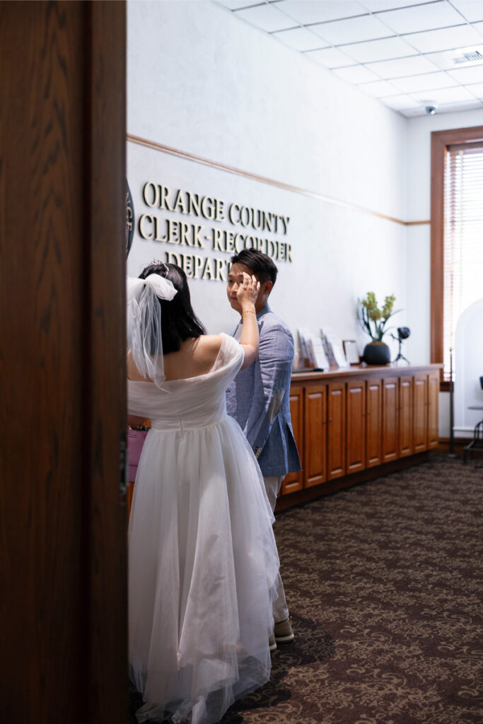 Bride sweeps hair from grooms forehead with her hand before city hall elopement in Orange County. 