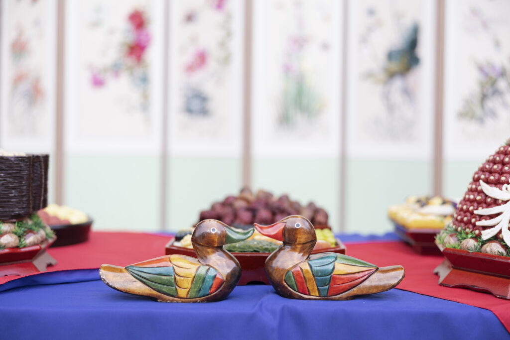 wooden ducks on a colorful table, part of a traditional Korean wedding setup with ceremonial treats