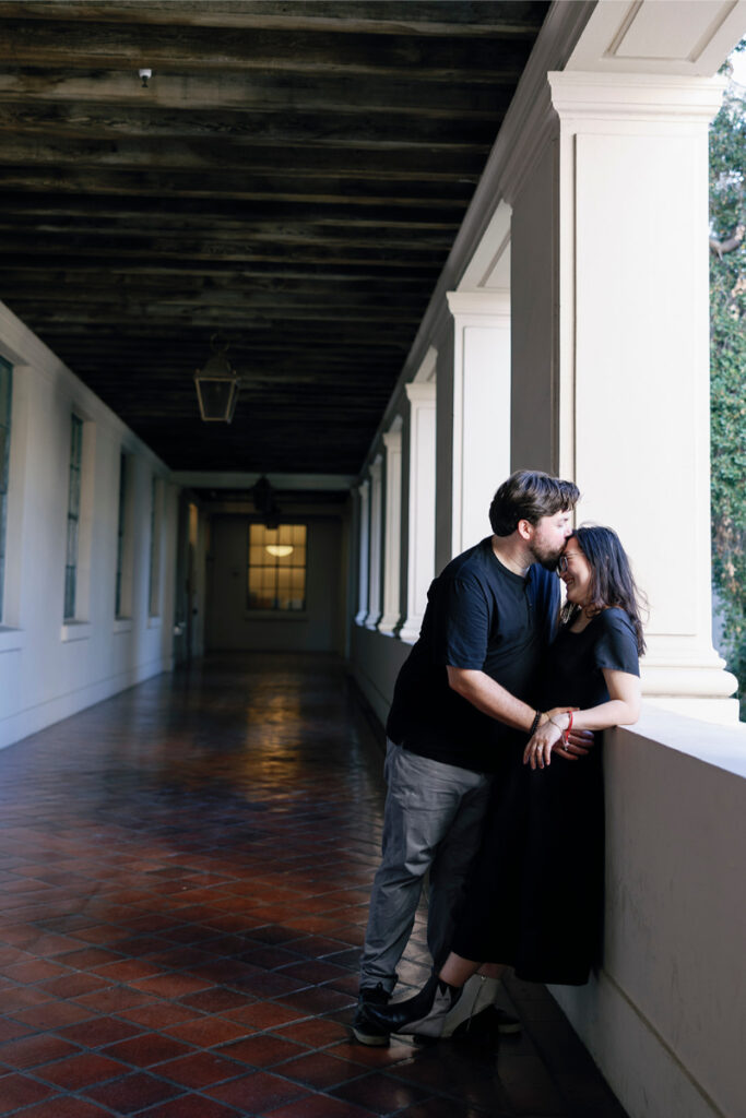 In a romantic moment, the groom kisses the bride on the forehead as they lean on a pillar-lined corridor at Pasadena City Hall.