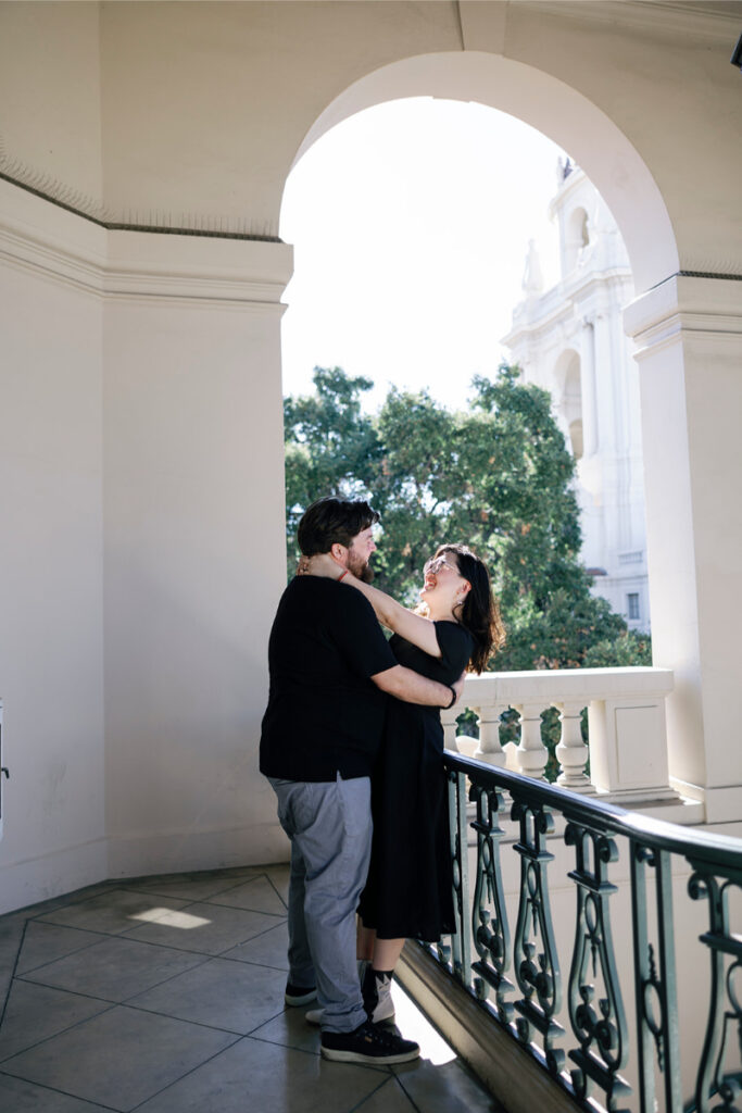 Standing beneath an elegant archway, the couple laughs together during their Pasadena City Hall elopement.