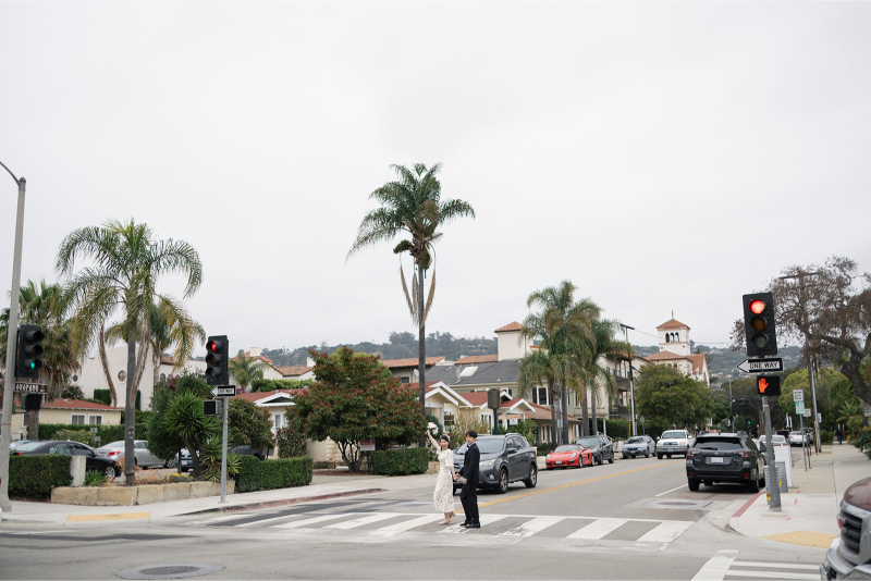 Bride and groom hold hands as they cross street together after elopement. 